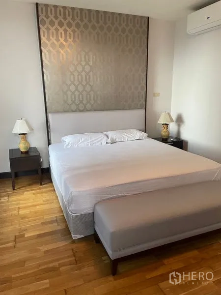 公寓 出租在Pathum Wan, Bangkok - 主卧，特大床、床尾长凳、床头灯与装饰床头板。