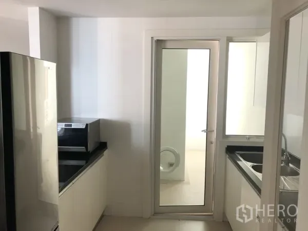 Condominium for rent in Khlong Toei, Bangkok - Bright separate kitchen with white cabinetry, black countertops, and a glass door to the utility area.