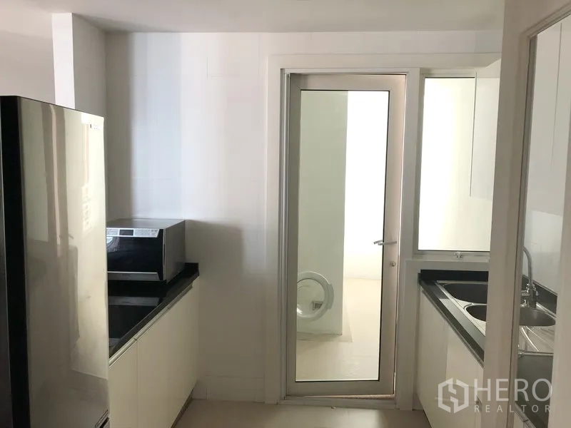 Condominium for rent in Khlong Toei, Bangkok - Bright separate kitchen with white cabinetry, black countertops, and a glass door to the utility area.