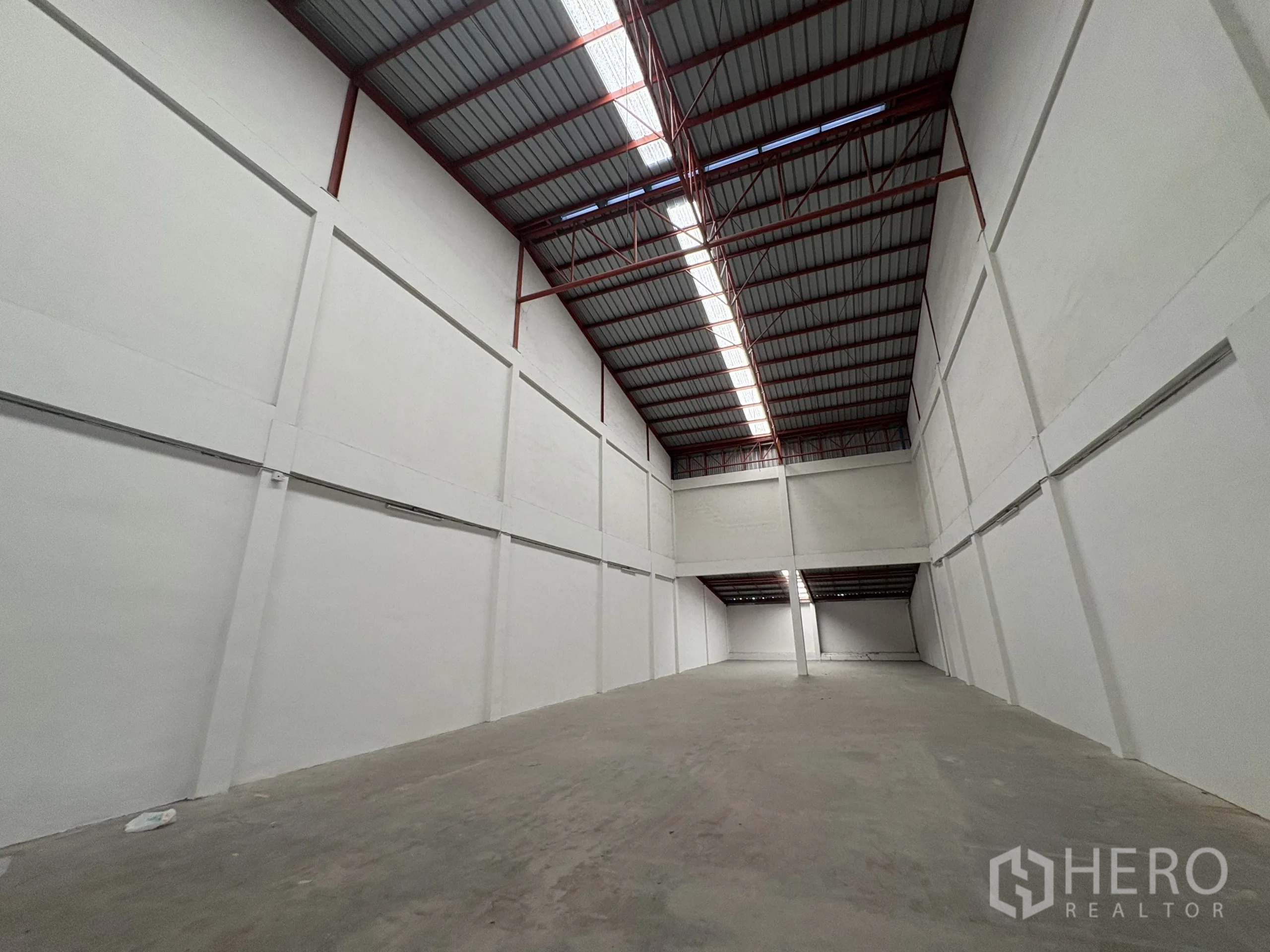 Factory for rent in Phra Samut Chedi, Samut Prakan - Long view of the warehouse showing skylights and tall white walls.