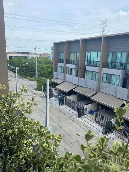 Townhouse for rent or sale in Saphan Sung, Bangkok - View from the balcony over a quiet townhouse street with greenery and neighboring facades.