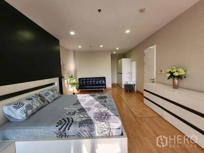 Condominium for rent in Khlong Toei, Bangkok - Large bedroom with seating area, dresser units and recessed lighting on timber floors.