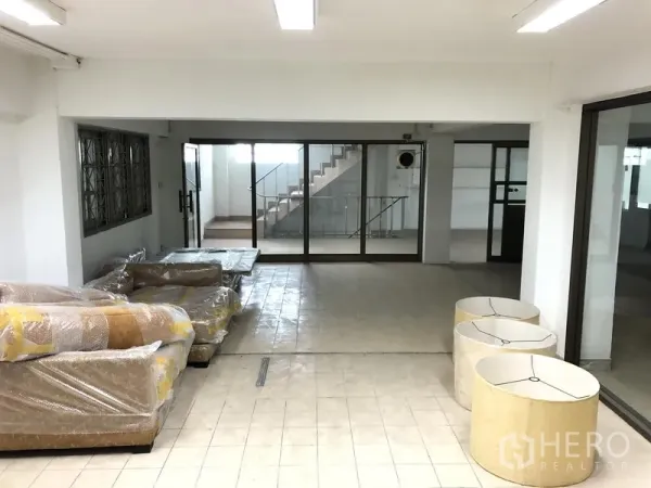 Office Space for rent in Huai Khwang, Bangkok - Ground-floor open area with tiled floor, wrapped furniture, glass doors and stair access.