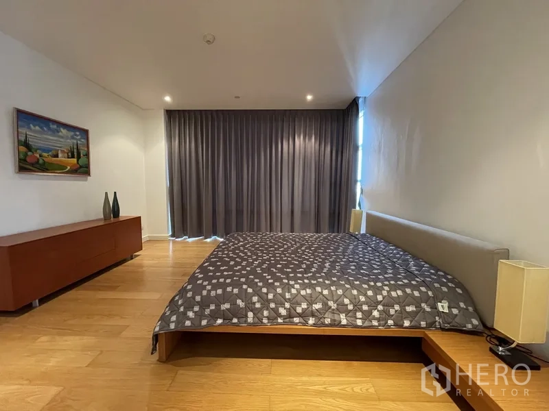 Condominium for rent or sale in Watthana, Bangkok - Primary bedroom front view with wide curtains, low sideboard, and warm wood flooring.