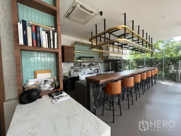 零售空间 出租在Watthana, Bangkok - 室内视角：长木质吧台、皮质高脚椅、开放式厨房与落地玻璃。