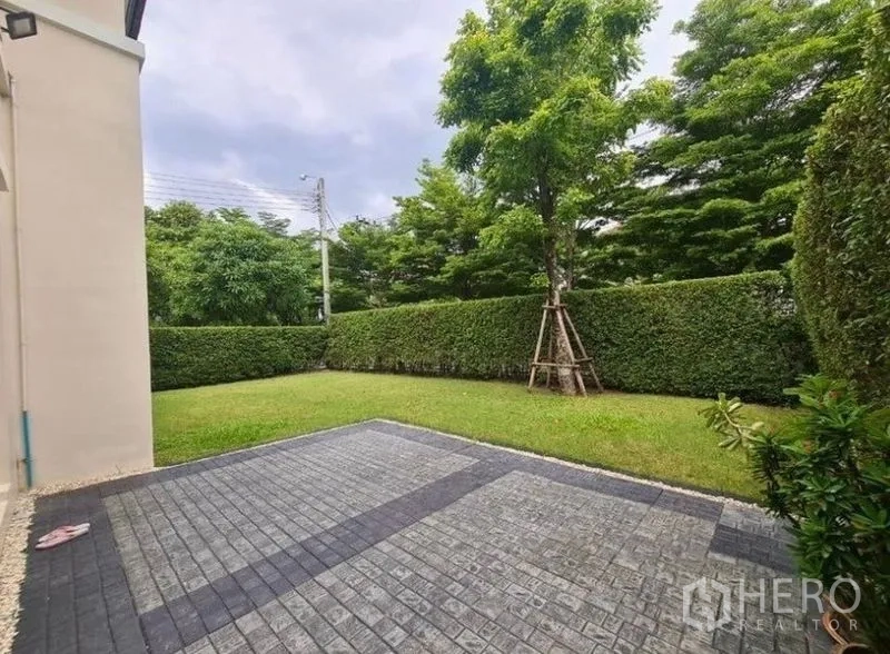 Detached House for rent or sale in Lat Krabang, Bangkok - Side garden with paved patio, trimmed hedge and trees creating a private outdoor area.