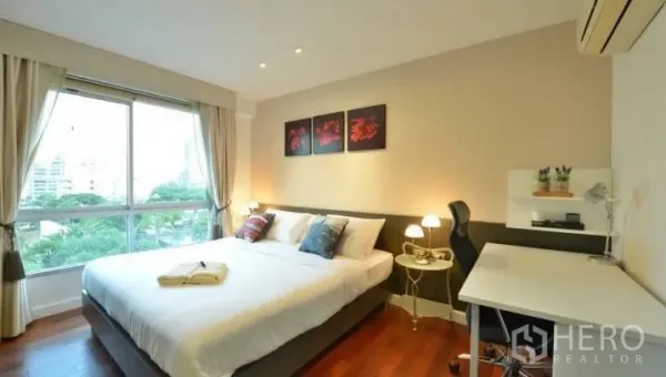 Condominium for rent in Watthana, Bangkok - Bright bedroom with king bed, large window with city and treetop views, wood floors and a work desk.