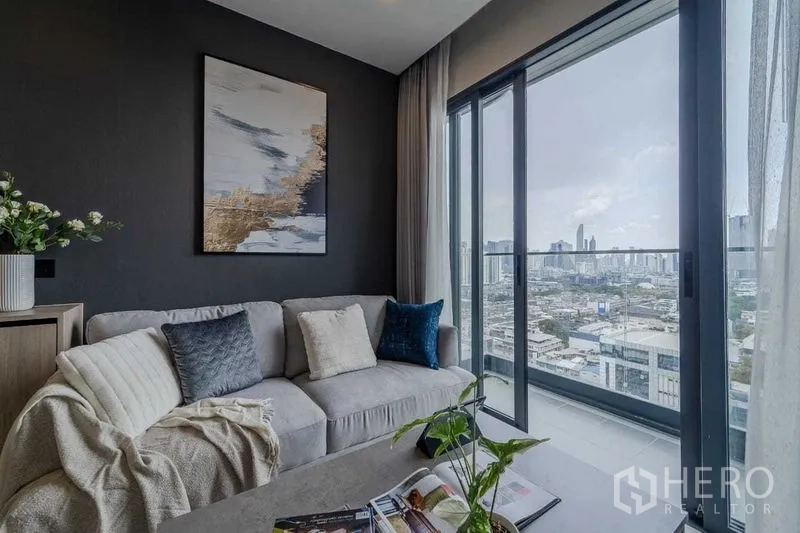 Condominium for rent in Pathum Wan, Bangkok - Modern living room with sofa beside sliding glass doors to the balcony and skyline outlook.