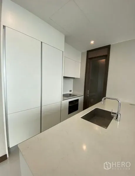 Condominium for rent in Khlong Toei, Bangkok - Sleek white kitchen with built-in cabinets, electric cooktop, oven and an island sink.