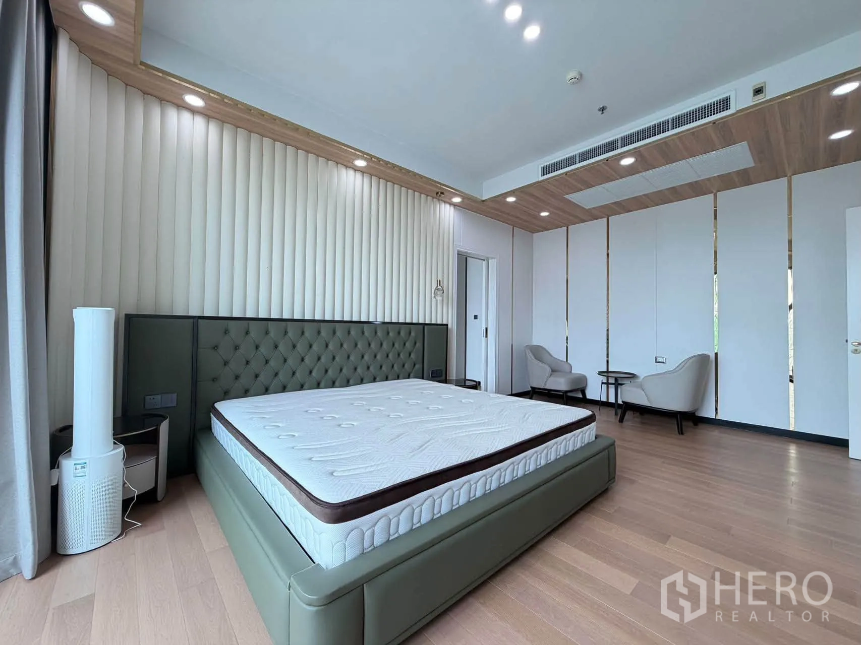 Condominium for sale in Watthana, Bangkok - Master bedroom with tufted headboard, seating area, and accent ceiling lights.