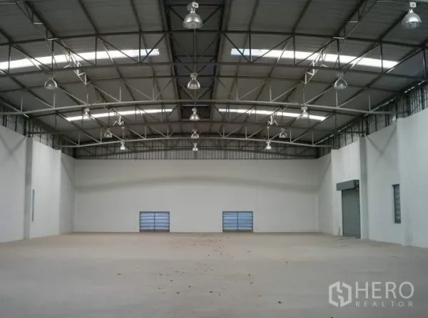 Factory for rent in Pathum Thani - Spacious warehouse interior with high steel truss roof, skylights, and smooth concrete floor.
