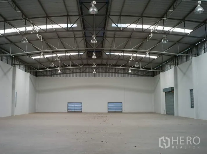 Factory for rent in Pathum Thani - Spacious warehouse interior with high steel truss roof, skylights, and smooth concrete floor.