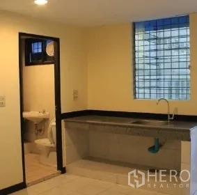 Office Space for rent in Bang Rak, Bangkok - Office pantry with long counter and sink beside an internal bathroom, under warm ceiling lights.