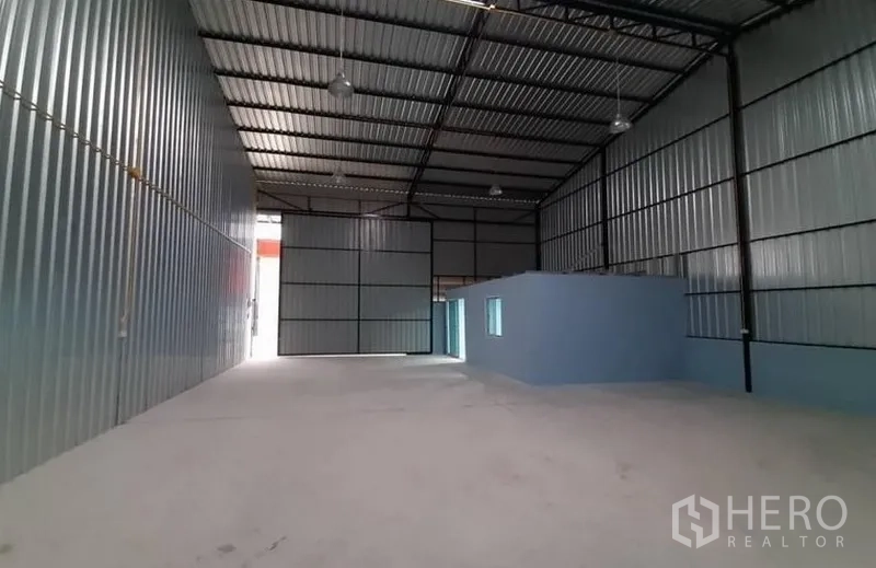 Warehouse for rent in Lam Luk Ka, Pathum Thani - Warehouse hall with hanging lights and a built‑in blue office room along the side wall.
