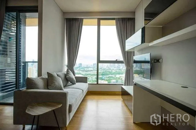 Condominium for rent in Khlong Toei, Bangkok - Living room with sofa, TV unit and floor-to-ceiling window facing green park views.