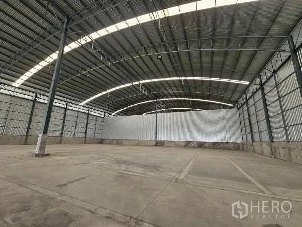Warehouse for rent in Lam Luk Ka, Pathum Thani - Open storage space under an arched steel roof with a central column, ideal for racking.