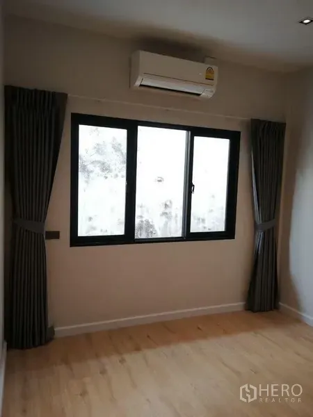 Townhouse for rent in Din Daeng, Bangkok - Air-conditioned bedroom with window and dark curtains over wood flooring.