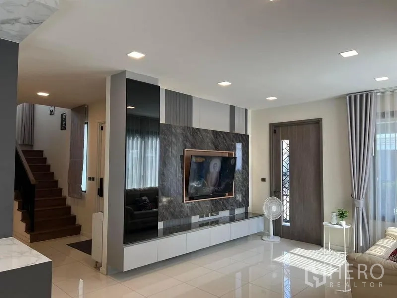 Detached House for rent or sale - Living room with marble TV wall, recessed lights and stair access.