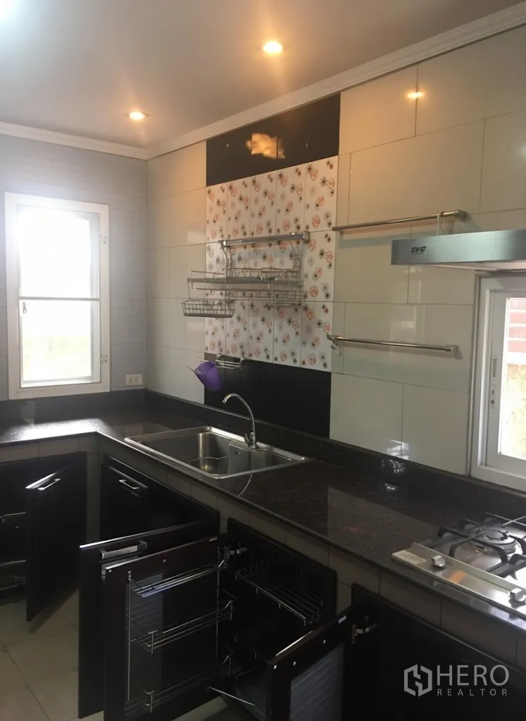 Detached House for rent in Lat Krabang, Bangkok - Kitchen close-up showing stainless sink, gas hob, tiled backsplash and open storage racks.