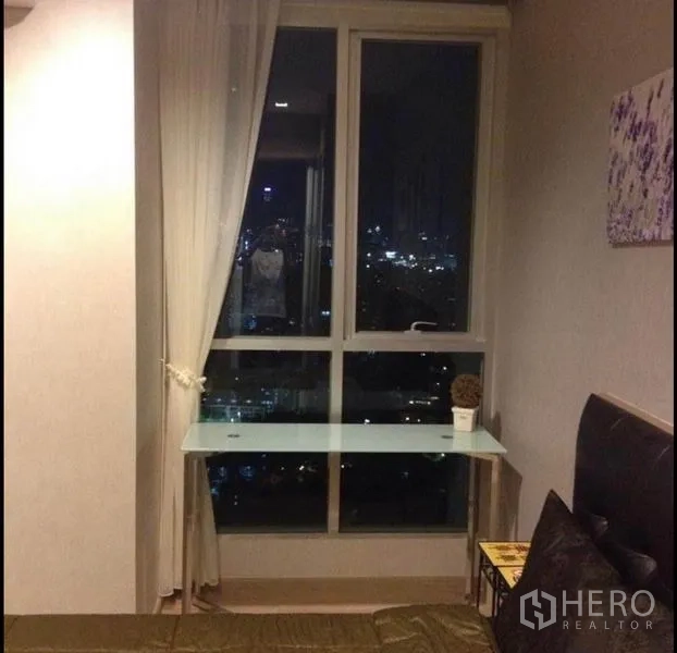 Condominium for sale in Phaya Thai, Bangkok - Bedroom corner with large window, sheer curtains, glass desk and night city view.