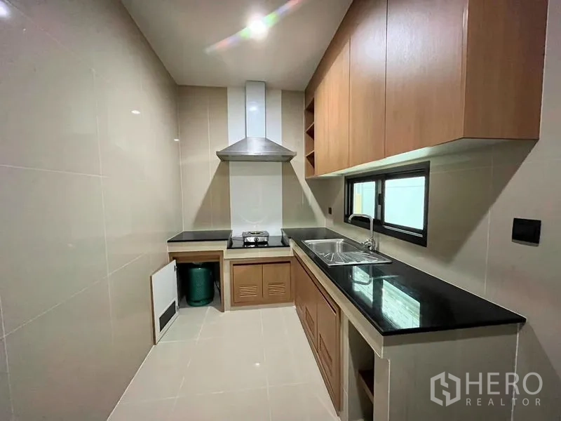 Detached House for rent in Bang Kapi, Bangkok - Closed kitchen with range hood, gas cooktop, black counters and cabinets
