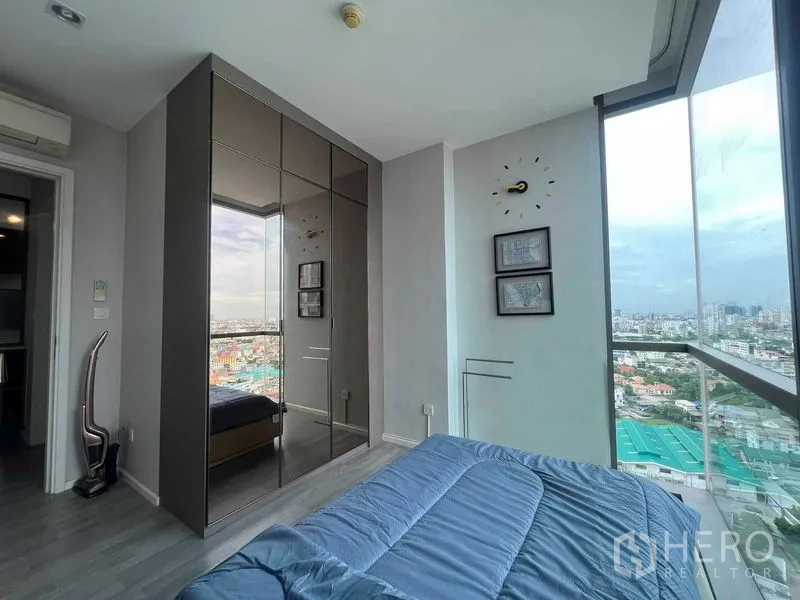 Condominium for rent in Khlong Toei, Bangkok - Corner bedroom with floor-to-ceiling windows and mirrored wardrobe overlooking the city.