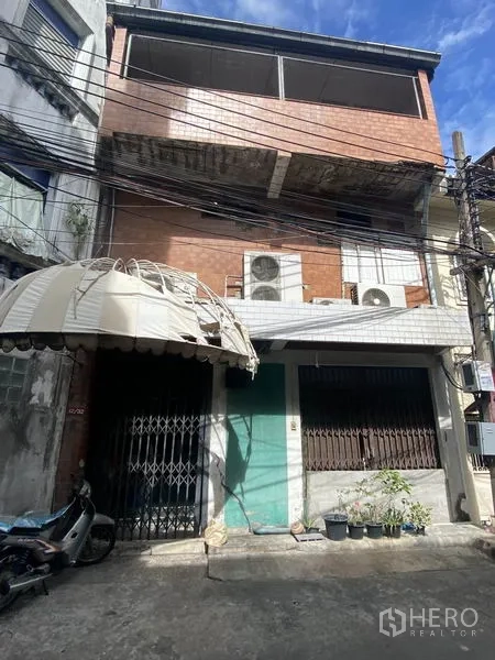 อาคารพาณิชย์ ขายในKhlong Toei, Bangkok - ด้านหลังอาคารพาณิชย์พร้อมประตูเหล็ก กันสาด และชุดคอมเพรสเซอร์แอร์ภายนอกขนาดใหญ่ ใต้ท้องฟ้าสีฟ้า เขตคลองเตย กรุงเทพฯ