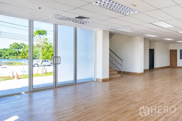 Warehouse for rent in Si Racha, Chon Buri - Open-plan office area with large glass entrance, ceiling lighting, and stairway access.