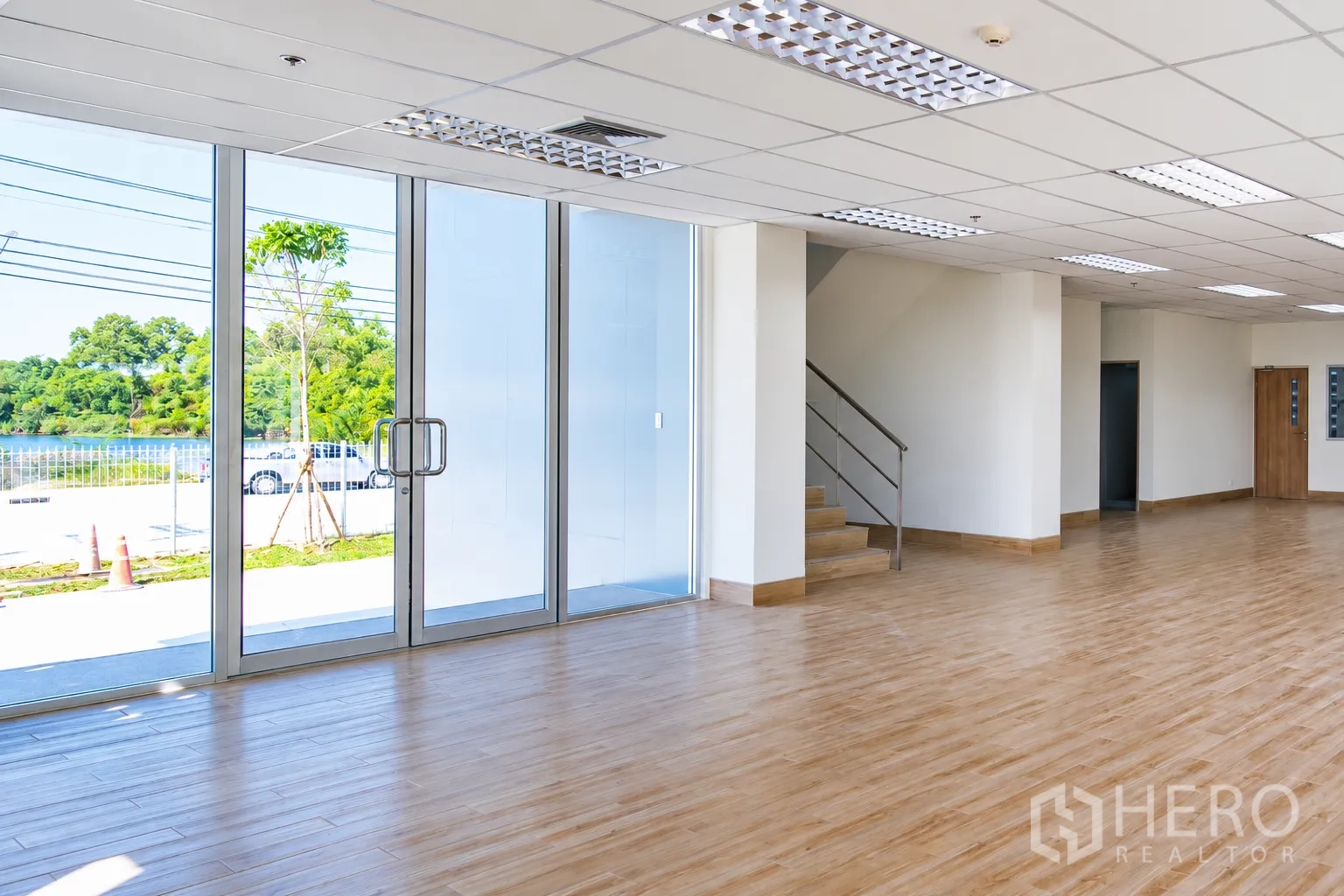 Warehouse for rent in Si Racha, Chon Buri - Open-plan office area with large glass entrance, ceiling lighting, and stairway access.