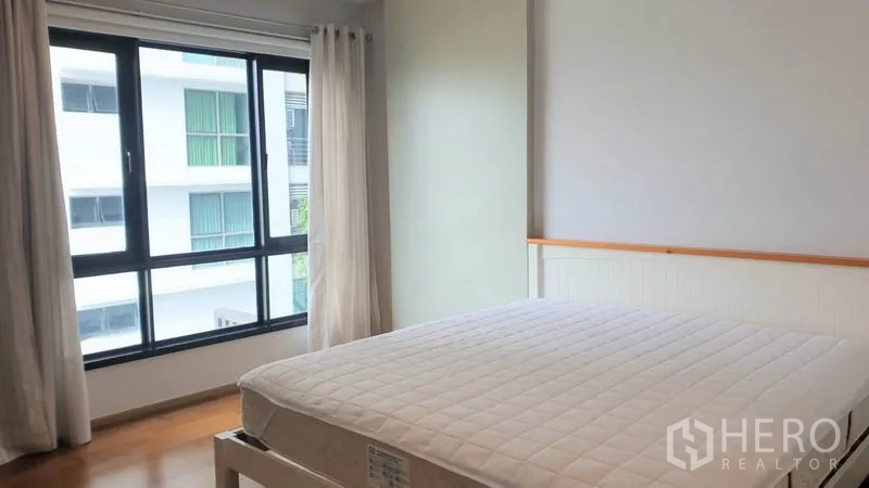Condominium for rent in Phaya Thai, Bangkok - Sunlit bedroom with large bed, wood floors and wide windows facing the neighboring building.
