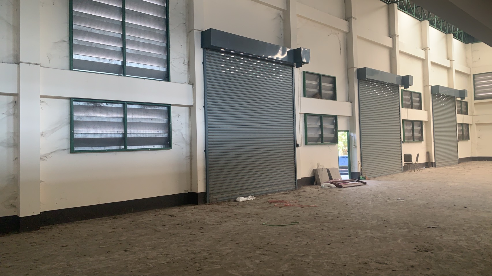 Warehouse for rent in Lam Luk Ka, Pathum Thani - Interior wall featuring multiple roller shutter doors and louvered ventilation windows.