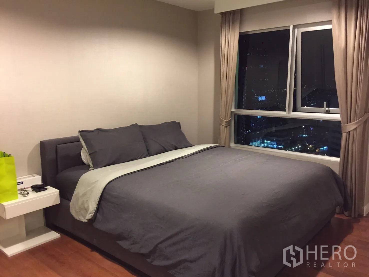 คอนโด ให้เช่าในHuai Khwang, Bangkok - ห้องนอนใหญ่เตียงคิงไซส์ พื้นไม้ และหน้าต่างบานใหญ่เห็นวิวสกายไลน์กรุงเทพฯ