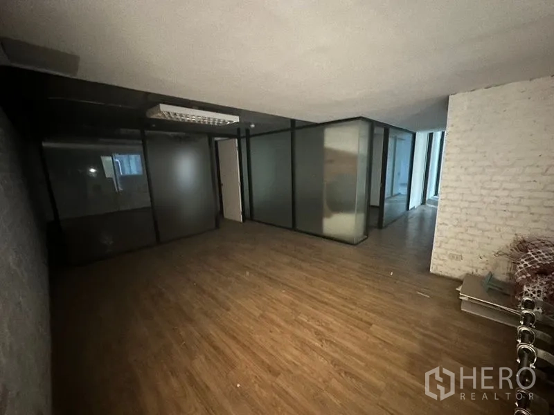 Office Space for rent in Khlong Toei, Bangkok - Open-plan workspace with wood flooring, frosted glass walls and a white brick accent wall.