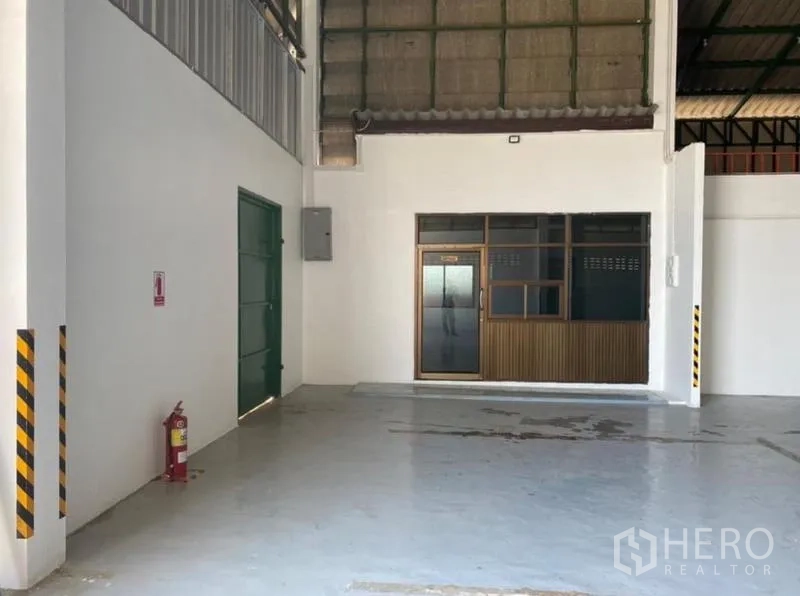 货栈 出租在Mueang Rayong, Rayong - 仓库一角，绿色服务门、灭火器与玻璃办公室。