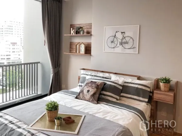 公寓 出租在Bang Rak, Bangkok - 舒适卧室，条纹床品与墙面置物架，临近阳台。