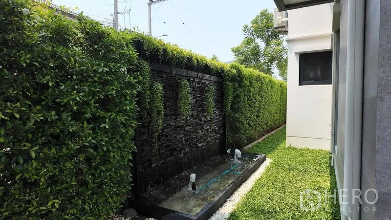 บ้าน ให้เช่าหรือขายในBang Na, Bangkok - สวนข้างบ้านพร้อมกำแพงน้ำตกหินและแนวรั้วต้นไม้ให้ความเป็นส่วนตัว