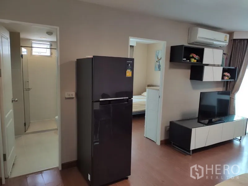 คอนโด ให้เช่าในHuai Khwang, Bangkok - มุมห้องนั่งเล่นเห็นชั้นวางทีวี ตู้เย็น และทางเข้าห้องน้ำกับห้องนอนอีกห้อง