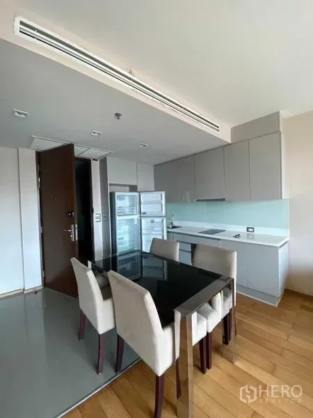公寓 出售在Ratchathewi, Bangkok - 开放式厨房，灰色柜体与玻璃防溅板，内置炉灶、立式冰箱及四人餐桌。