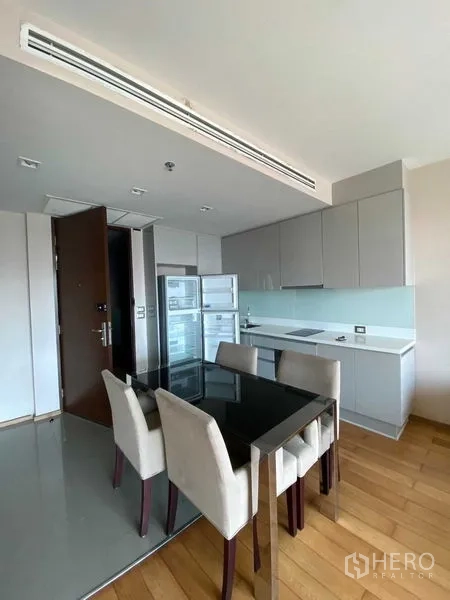 公寓 出售在Ratchathewi, Bangkok - 开放式厨房，灰色柜体与玻璃防溅板，内置炉灶、立式冰箱及四人餐桌。