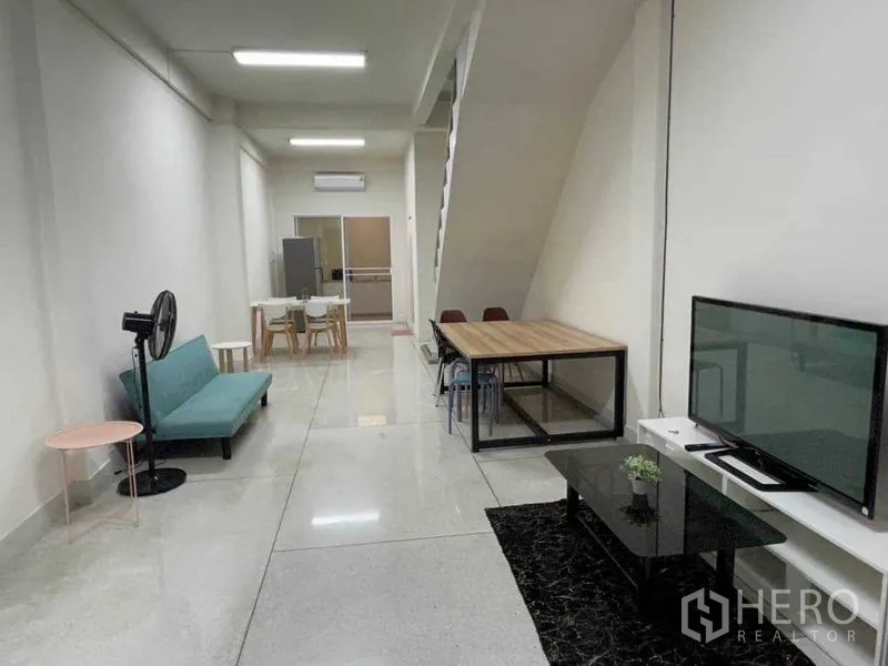 带办公室的家 出租或出售在Watthana, Bangkok - 开放式客厅，设沙发、电视、餐桌与楼梯，空间狭长。