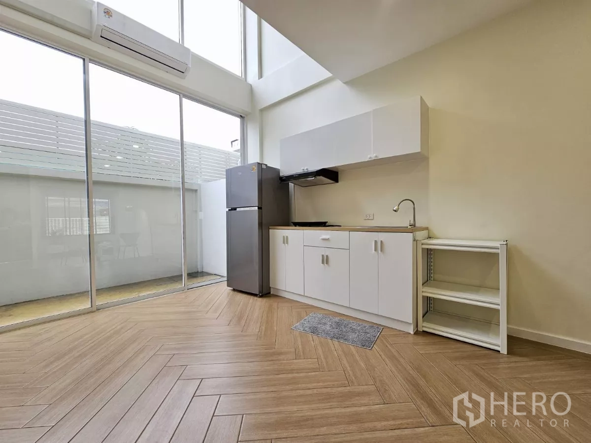 Townhouse for sale in Lat Phrao, Bangkok - Compact kitchenette with tall glass wall, herringbone wood floor and double-height ceiling.