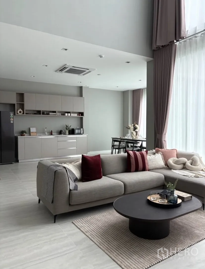 บ้านเดี่ยว for rent in Suan Luang, Bangkok - ห้องนั่งเล่นเพดานสูงสว่าง โซฟาตัวยาว พร้อมม่านสูง และครัวแพนทรี่สไตล์มินิมอล