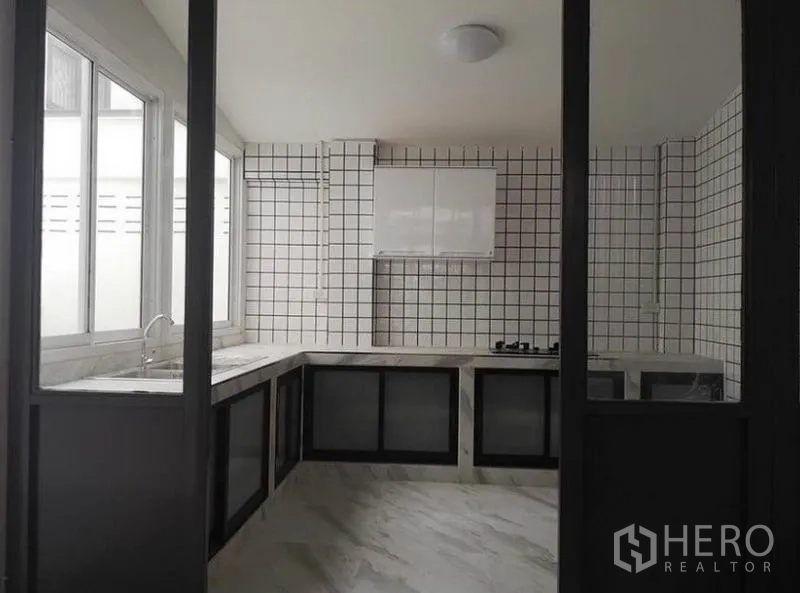 Townhouse for rent or sale in Din Daeng, Bangkok - Enclosed kitchen with U-shaped marble-look counters, tiled walls, gas cooktop, and large windows.