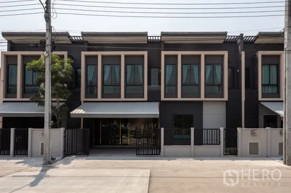Townhouse for rent in Bang Phli, Samut Prakan - Modern two-storey townhouse facade with large windows, gated frontage and a shaded driveway.