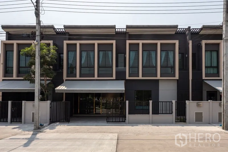 联排别墅 出租在Bang Phli, Samut Prakan - 现代两层联排外立面，大窗与前庭围栏，带遮阳篷