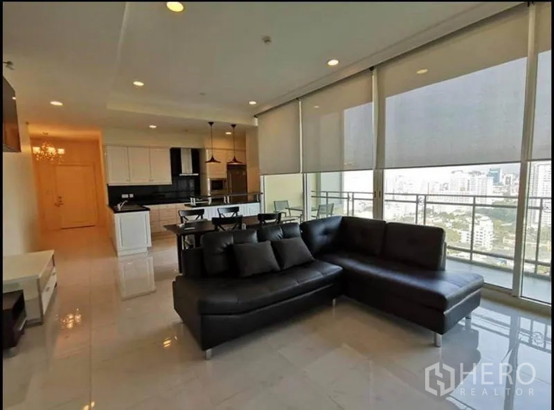 Condominium for rent in Watthana, Bangkok - Open-plan living and dining area with L-shaped leather sofa and wall-to-wall windows.