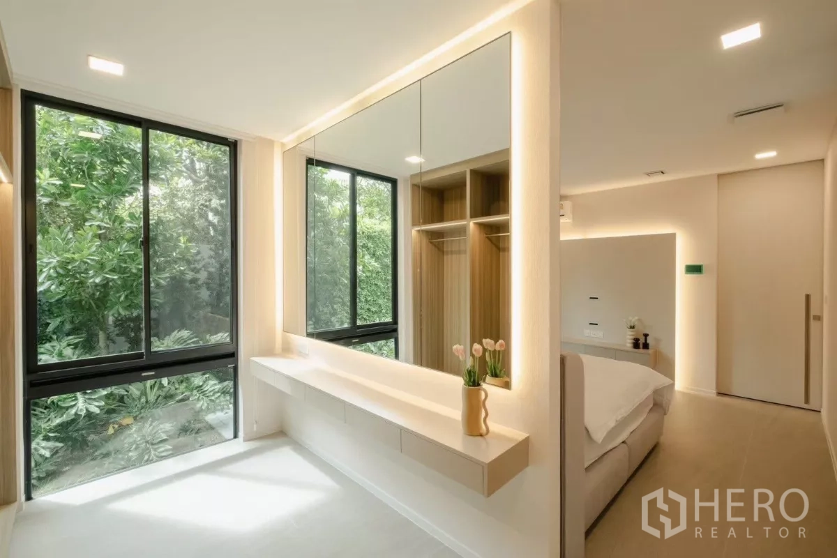 Detached House for rent in Saphan Sung, Bangkok - Dressing area with large mirrors, picture windows to greenery, built‑in vanity, and open wardrobe beside the bedroom.