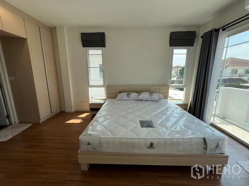 独立式住宅 出租在Bang Kapi, Bangkok - 主卧配大窗与阳台推拉门，浅木色床架。