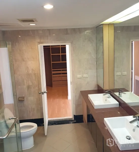 Condominium for rent in Watthana, Bangkok - Bathroom with glass-enclosed shower, twin sinks and door to a walk-in closet.