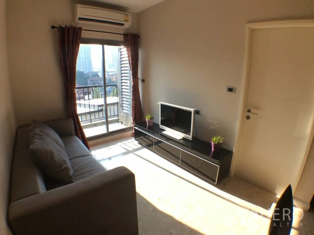 Condominium for rent in Khlong Toei, Bangkok - Bright living room with sliding door to a small balcony, air conditioner, and TV stand.